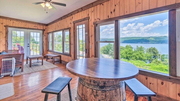 A wooden cabin with a large round table, benches, and a ceiling fan.