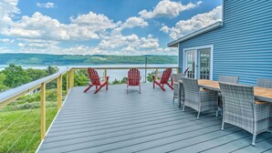 A deck with outdoor furniture, a view of a lake, and a house in the background.