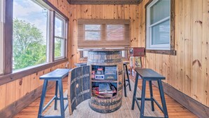 A wooden interior with a barrel fireplace, wooden walls, and large windows.