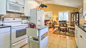 A kitchen with white cabinets, a microwave, a refrigerator, and a stove. There is a dining area with a table and chairs.