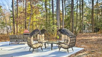 A patio with wicker chairs and a table, surrounded by trees.