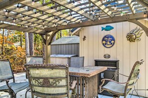 Une terrasse extérieure avec une pergola en bois, une table et des chaises. Il y a une enseigne sur le mur où l’on peut lire : « John’s Tiki Bar ».