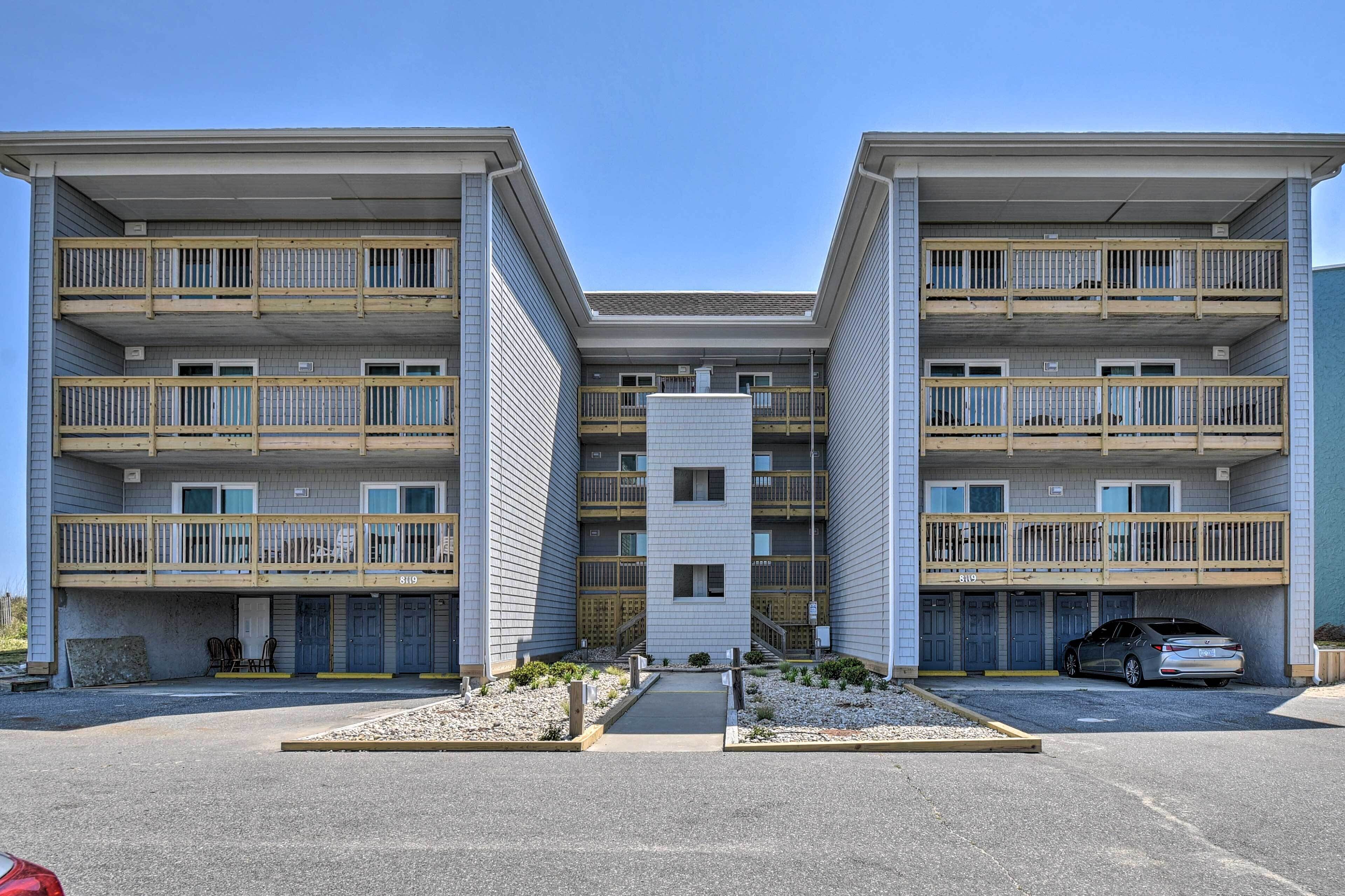 A modern multi-story building with a central courtyard, balconies, and a parking area.