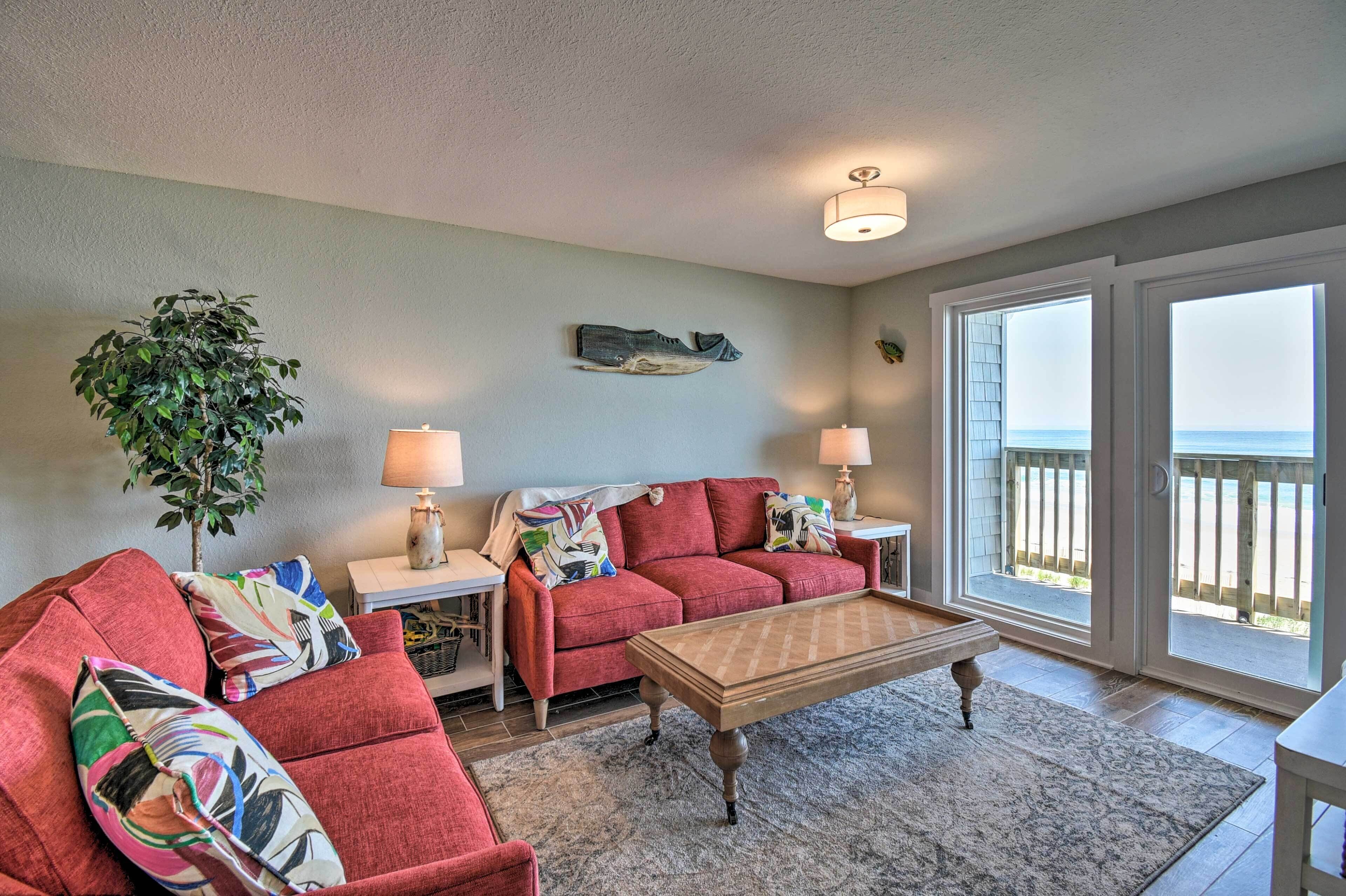 A living room with a red sofa, a wooden coffee table, and a view of the ocean through large sliding glass doors.
