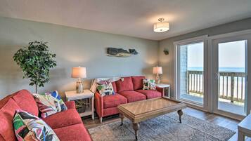 A living room with a red sofa, a wooden coffee table, and a view of the ocean through large sliding glass doors.