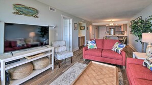 A living room with a flat-screen TV, a red sofa, a white armchair, and a coffee table. - Beachfront Nags Head Condo w/ Private Balcony! (Nags Head)