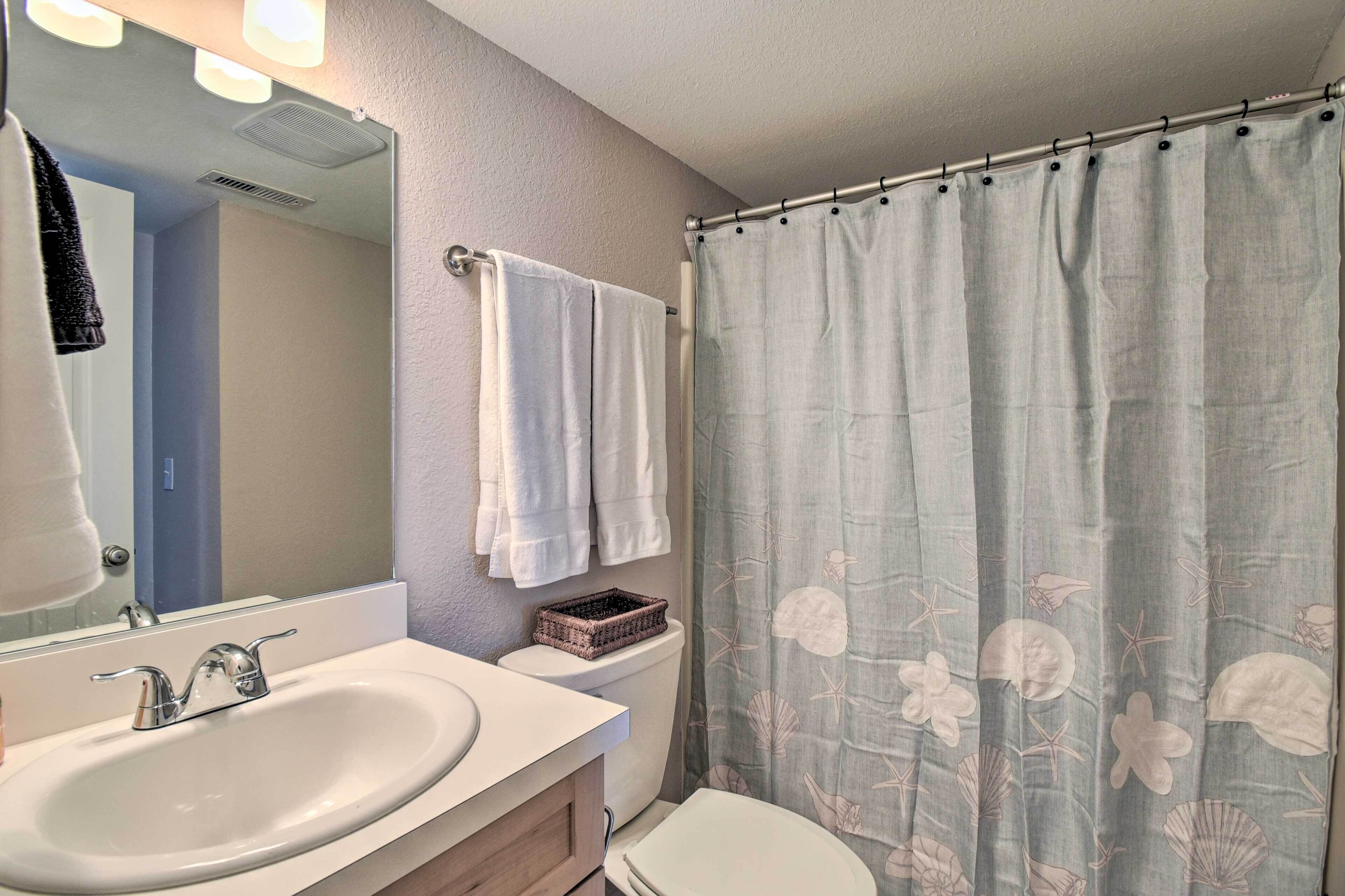 A bathroom with a white sink, a mirror, a toilet, and a shower curtain with a floral pattern.