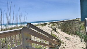 A beach with a wooden walkway leading to the ocean, sandy dunes, and a clear blue sky. - Beachfront Nags Head Condo w/ Private Balcony! (Nags Head)
