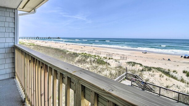 A wooden deck overlooking a beach with a pier in the distance. - Beachfront Nags Head Condo w/ Private Balcony! (Nags Head)