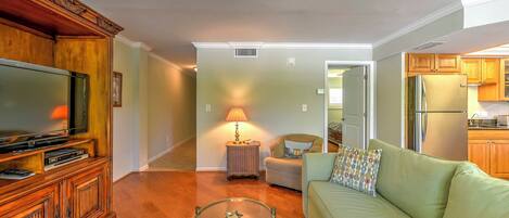 A living room with a television, wooden cabinet, glass coffee table, and a green sofa.