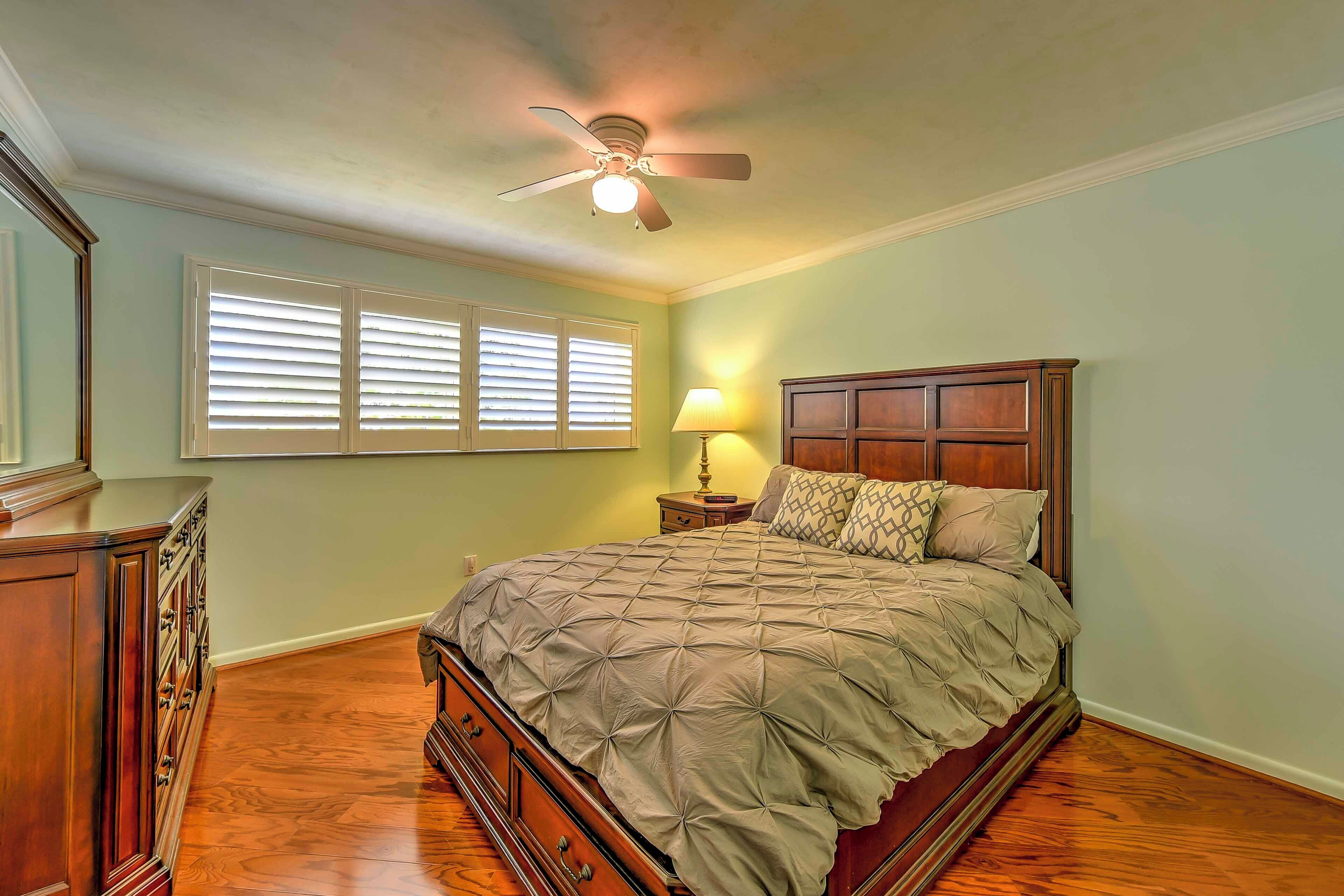 Une chambre à coucher avec un lit en bois, un ventilateur de plafond, une table de chevet avec une lampe et une commode.