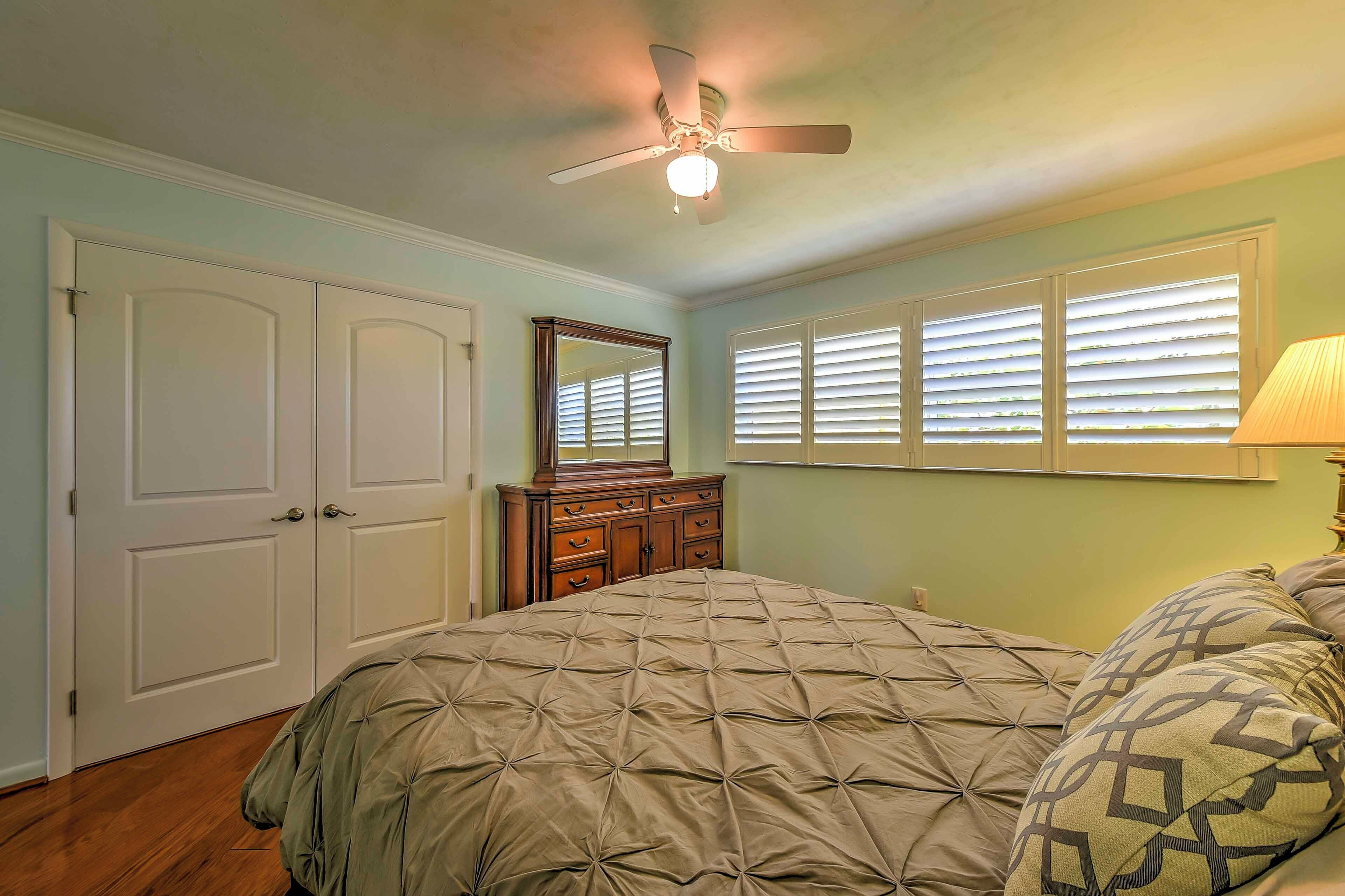 Un dormitorio con cama, cómoda, ventilador de techo y ventana con persianas.