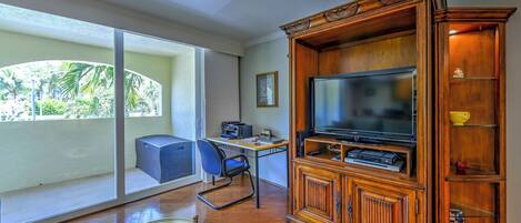 Ein geräumiges Wohnzimmer mit großem Fernseher, einer Holzeinrichtungsanlage und Blick auf einen Balkon mit Stuhl und Tisch.