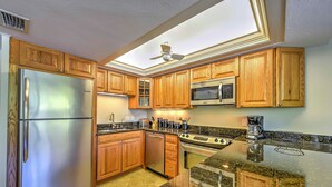 A kitchen with wooden cabinets, stainless steel appliances, a ceiling fan, and a granite countertop. - Marco Island Condo w/ Patio: Steps to Beach Access (Marco Island)