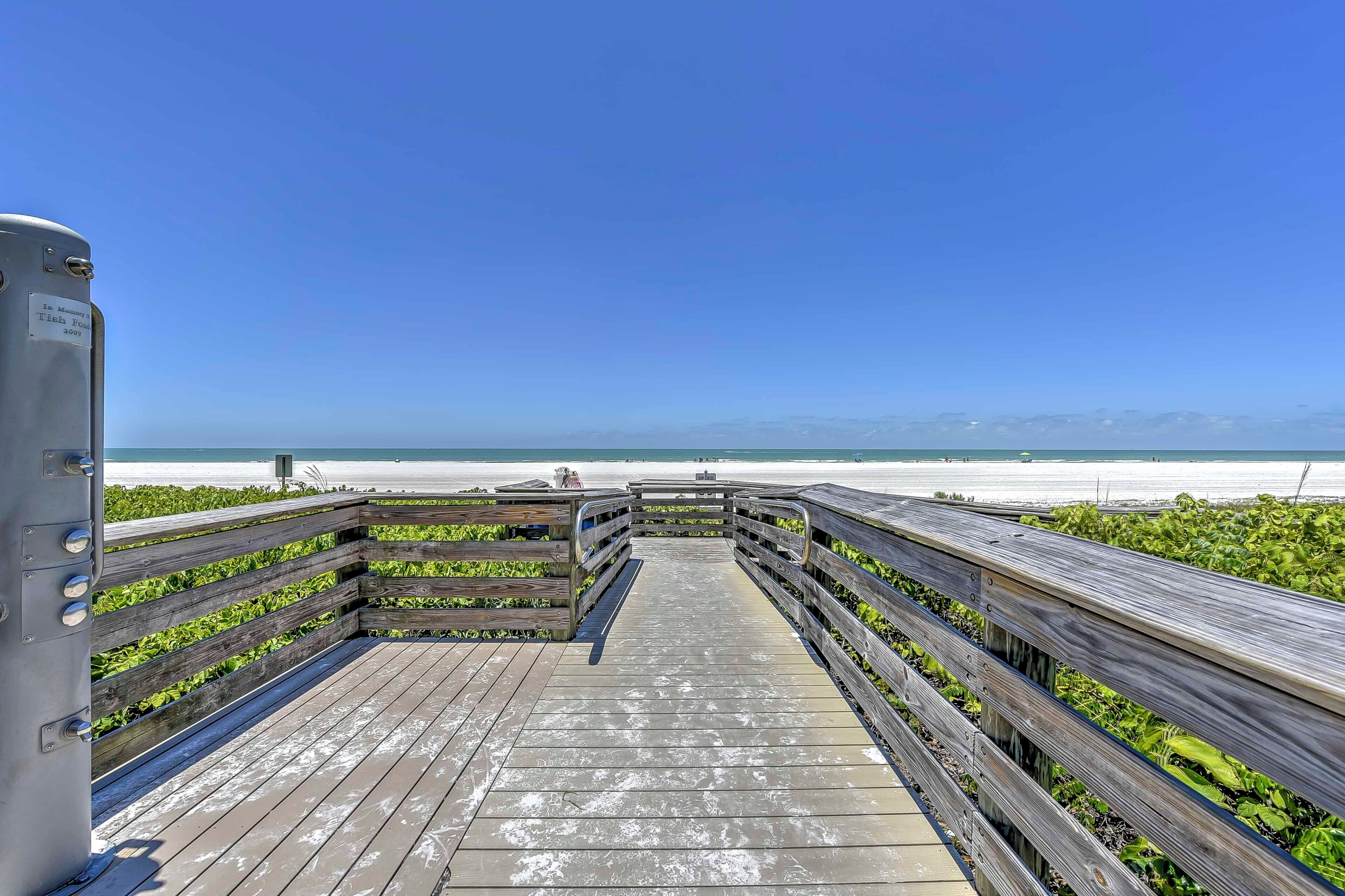 A wooden boardwalk leading to a beach with a clear view of the ocean and distant mountains.