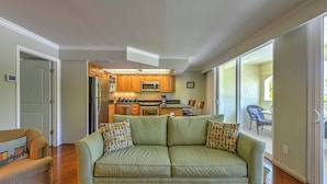 A living room with a green sofa, a wooden dining table, and a kitchen in the background. - Marco Island Condo w/ Patio: Steps to Beach Access (Marco Island)