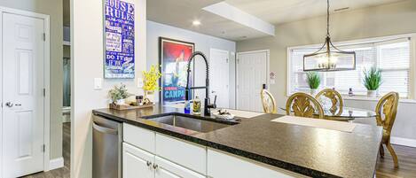 A kitchen with white cabinets, a granite countertop, a stainless steel dishwasher, and a dining area with a glass table and wooden chairs.