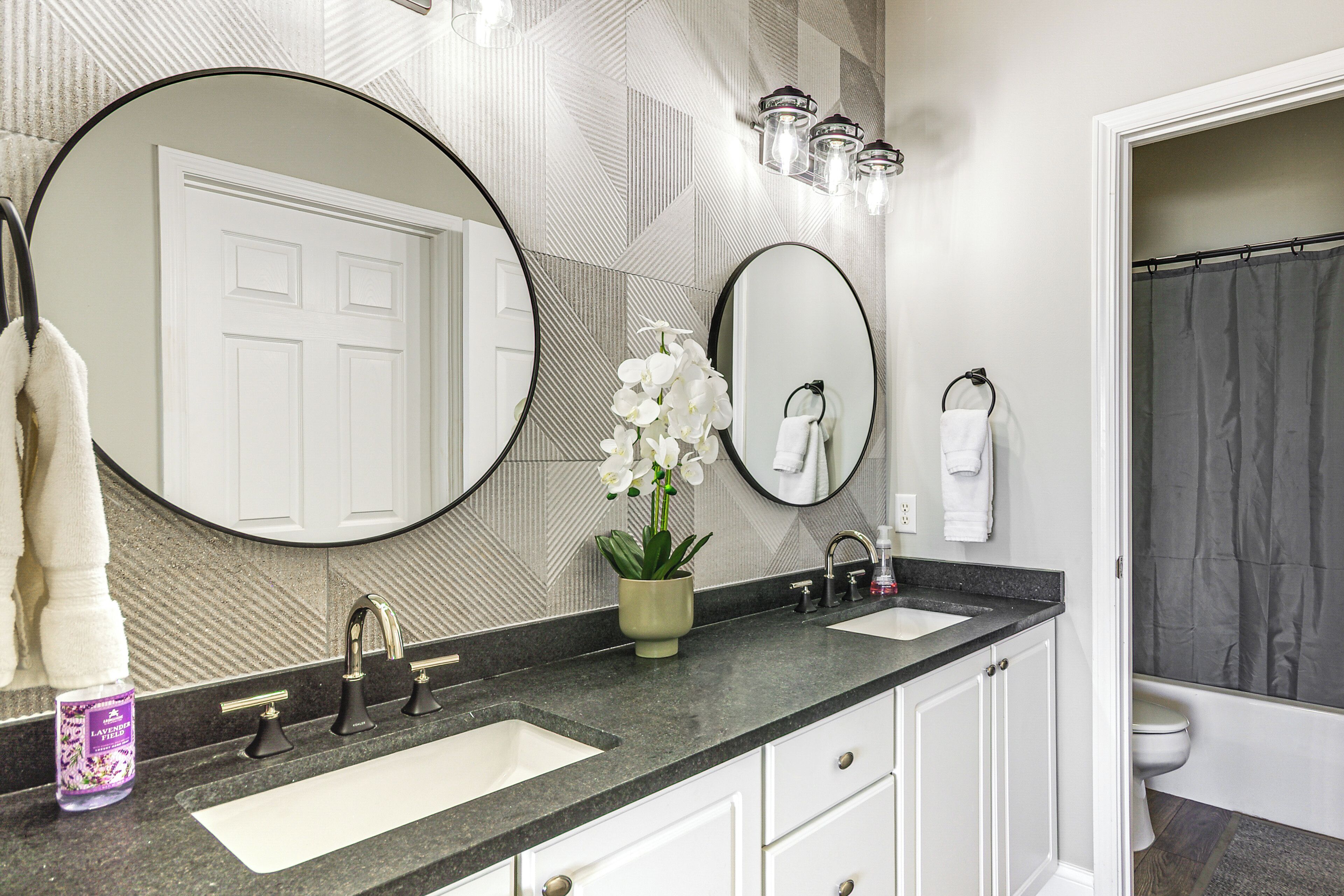 A bathroom with two sinks, a large mirror, a potted orchid, and a shower curtain.