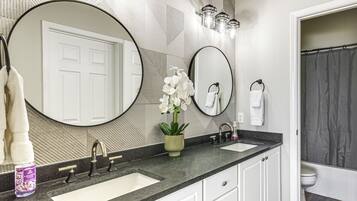 A bathroom with two sinks, a large mirror, a potted orchid, and a shower curtain.
