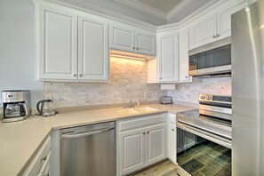 Una cocina moderna con armarios blancos, horno empotrado y refrigerador de acero inoxidable.