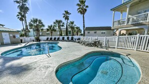A swimming pool with two distinct sections, surrounded by lounge chairs and a white fence. - Sunny PCB Home w/ Balcony: Steps to the Beach! (Panama City Beach)