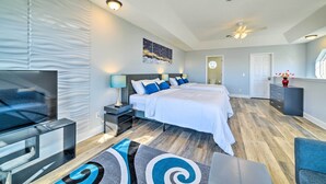 A modern bedroom with a large bed, a TV, and a ceiling fan. - Sunny PCB Home w/ Balcony: Steps to the Beach! (Panama City Beach)