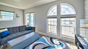 A modern living room with a grey sectional sofa, a bench, and a large window with a view of buildings. - Sunny PCB Home w/ Balcony: Steps to the Beach! (Panama City Beach)