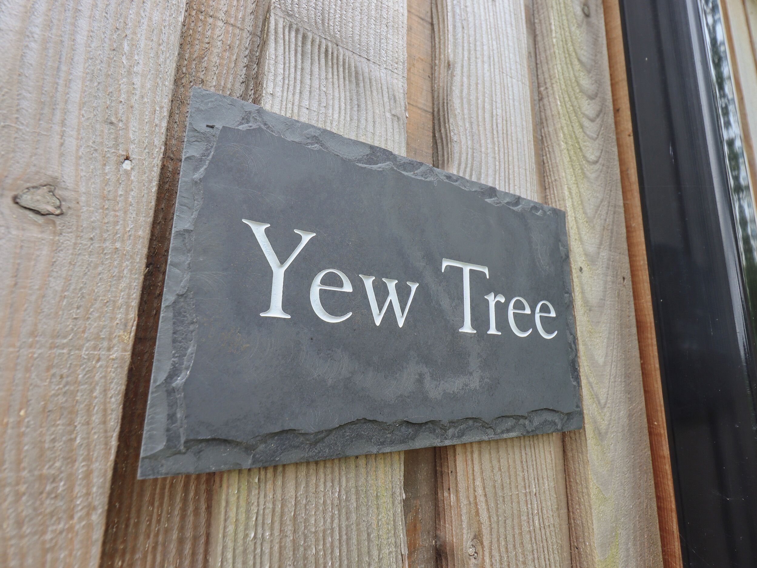 Un letrero de pizarra con el texto 'Yew Tree' sujeto a una superficie de madera.