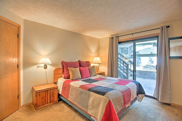 A bedroom with a bed, two bedside lamps, a nightstand, and a view of the outside through a sliding glass door. - Sunriver Home w/ Hot Tub & 8 Sharc Passes (Bend)