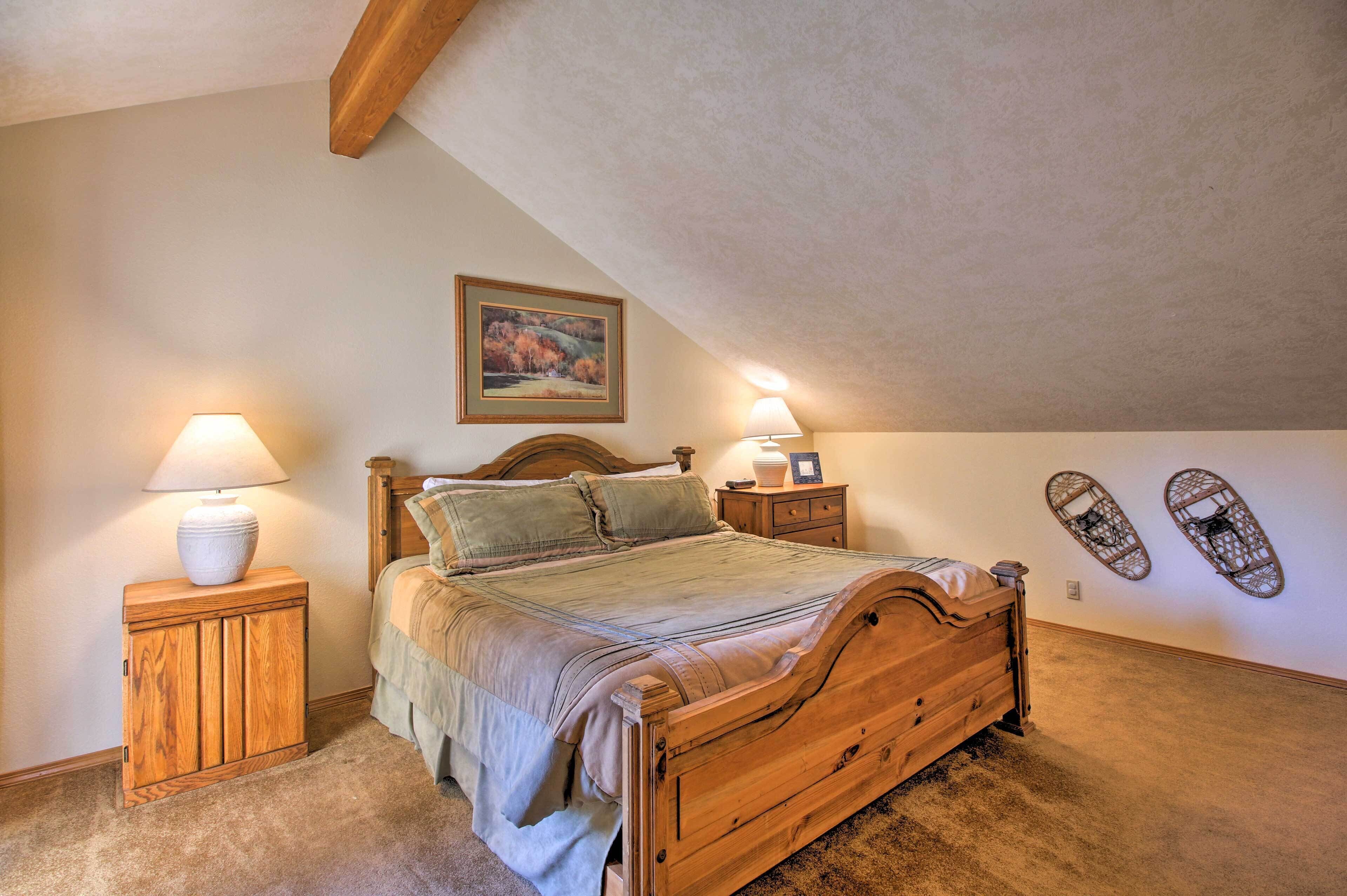 A bedroom with a wooden bed, two bedside tables with lamps, a painting on the wall, and two wall-mounted decorations.