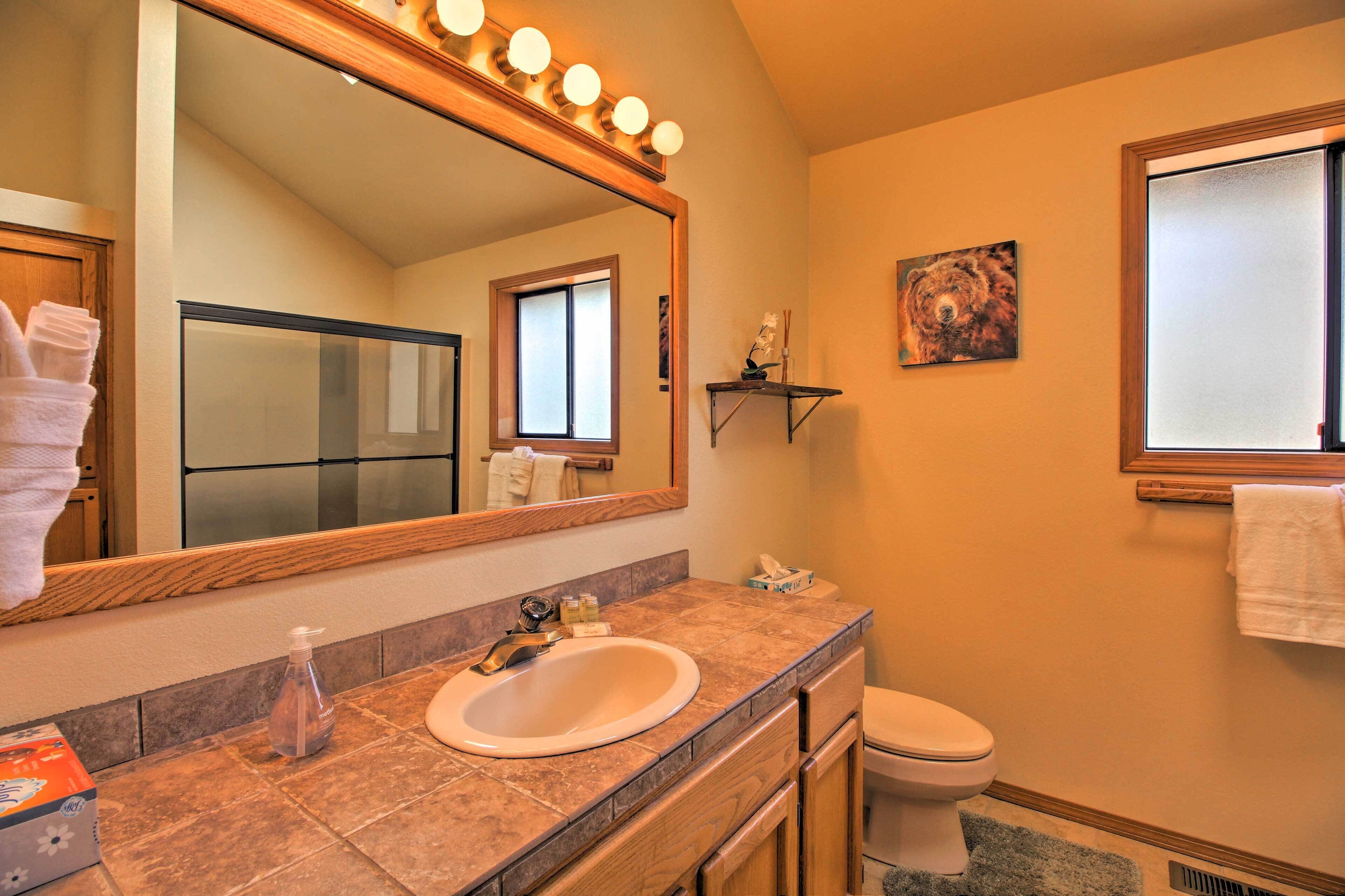 A bathroom with a large mirror, a sink, a toilet, and a window.