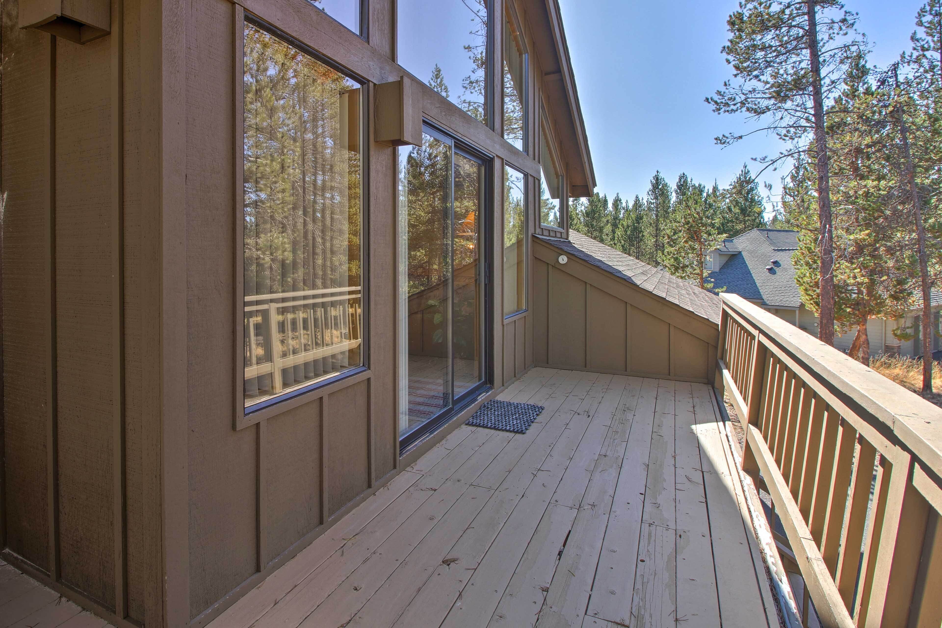 A wooden deck with a glass door leading to a covered area, surrounded by trees.