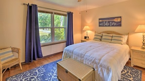 A bedroom with a bed, a window with curtains, a ceiling fan, a lamp, and a wicker chest. - Grand Lake Views + Fire Pit: Monkey Island Home! (Afton)