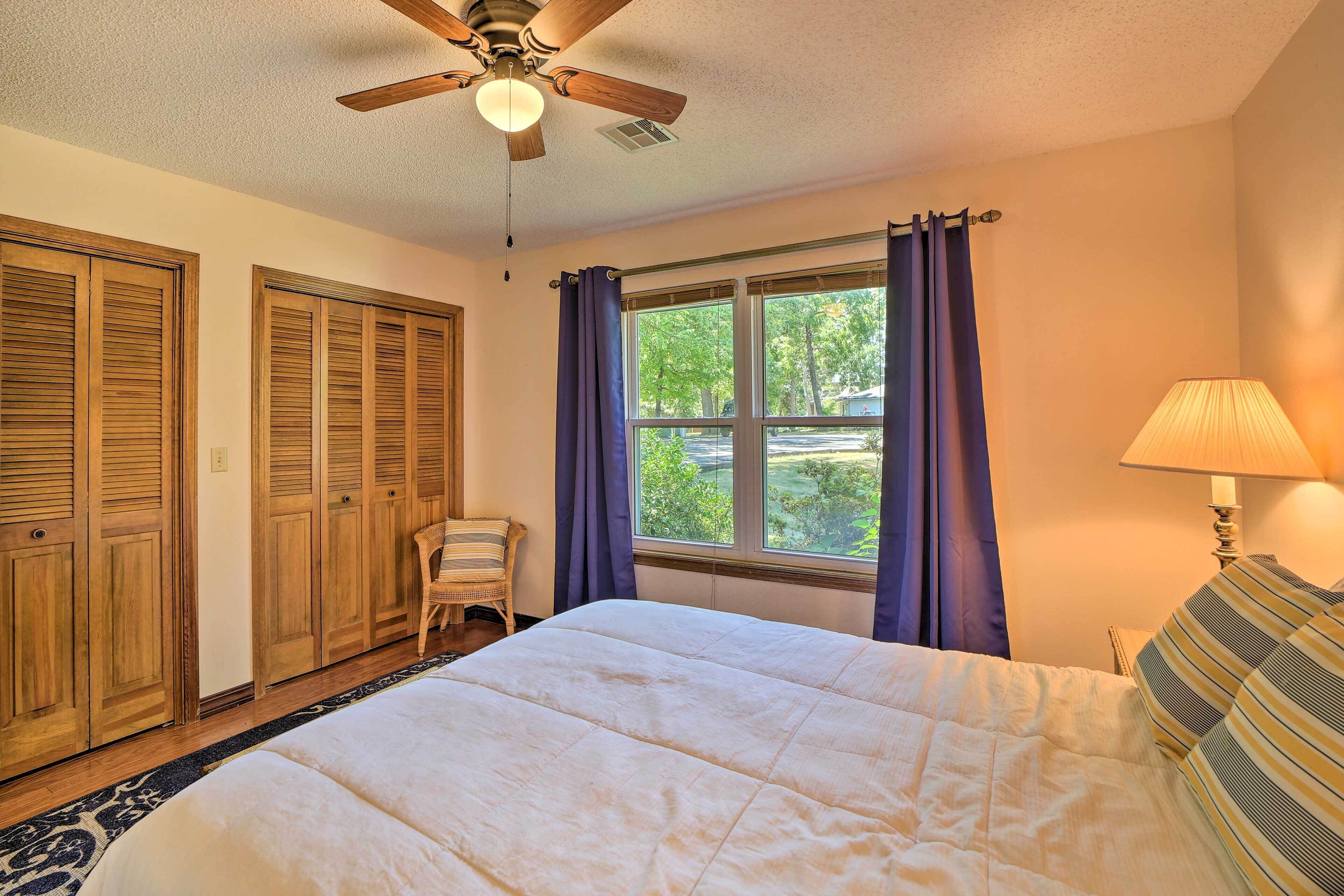 A bedroom with a bed, a ceiling fan, a window with curtains, and a lamp.