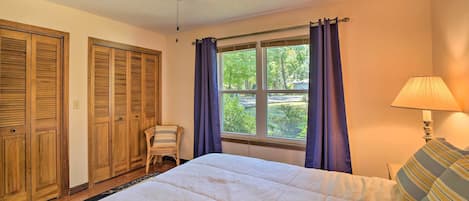 A bedroom with a bed, a ceiling fan, a window with curtains, and a lamp.