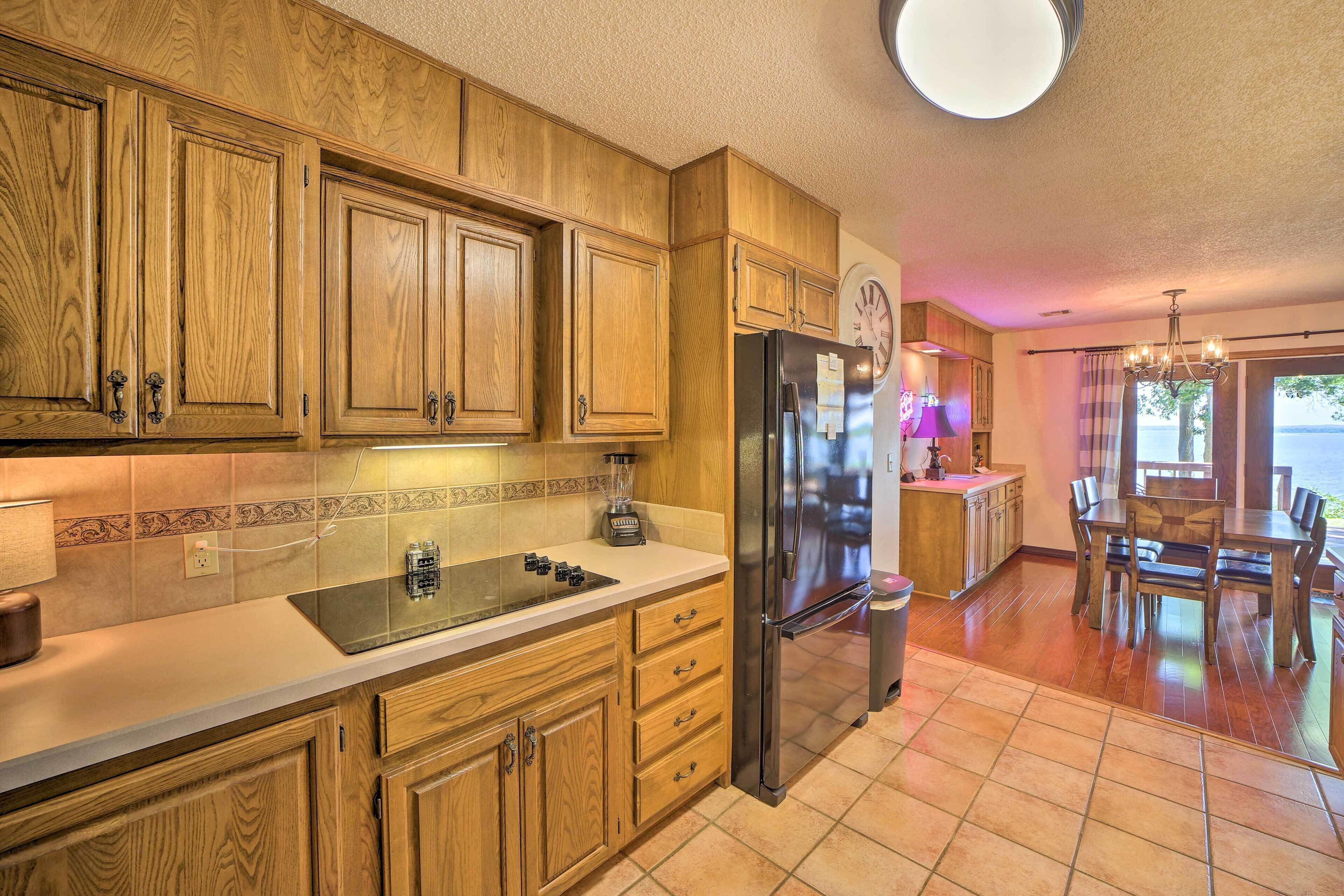 A kitchen with wooden cabinets, a stainless steel refrigerator, a blender on the counter, and a dining area with a table and chairs.