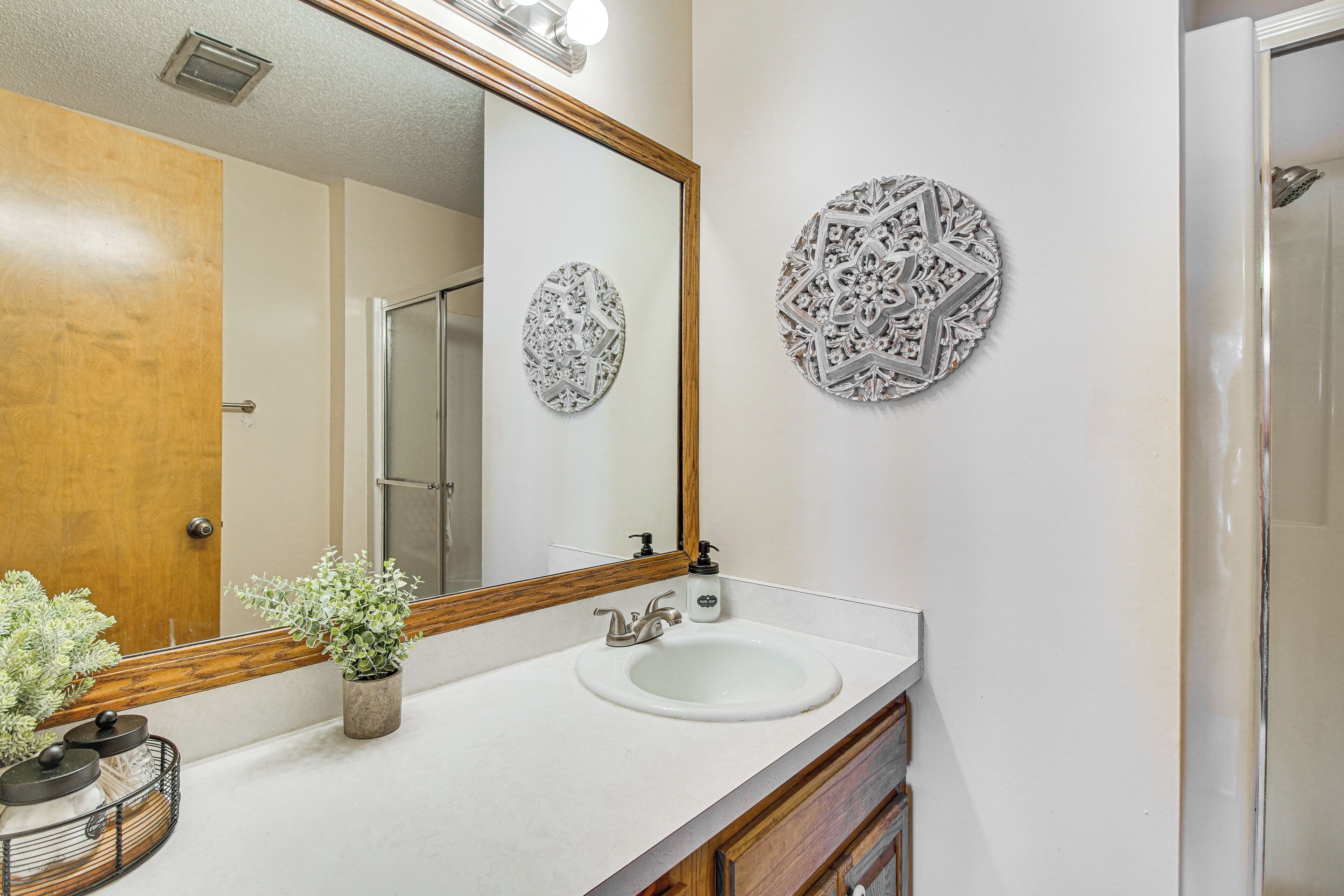 Un baño con puerta de madera, un lavamanos blanco, un espejo con marco de madera y detalles decorativos en la pared.