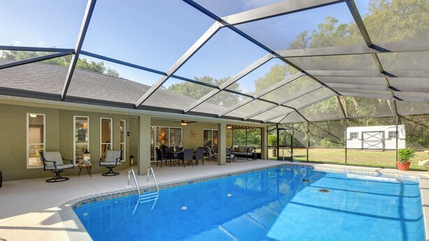 An indoor swimming pool with a glass ceiling, surrounded by lounge chairs and a patio area. - 8 Mi to Rainbow Springs: Dunnellon Area Home! (Citrus Springs)
