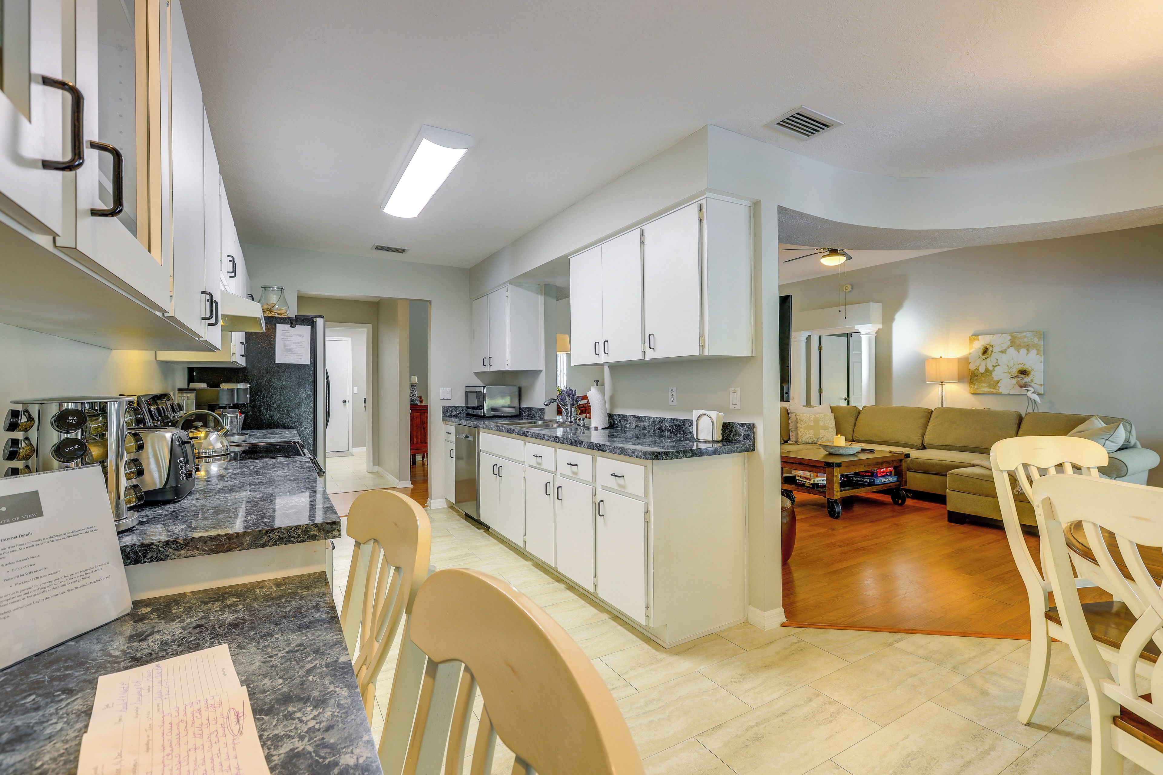 A modern kitchen with white cabinets, a granite countertop, and a dining area with wooden chairs.