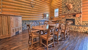 Interior de una cabaña de troncos con chimenea de piedra, mesa de comedor de madera y sillas.