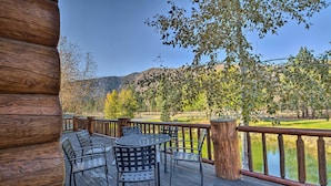 Una terraza de madera con mobiliario exterior, con vistas a un lago y colinas.