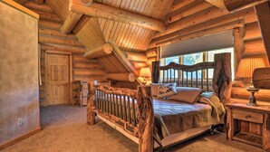 Un dormitorio de cabaña de madera con una cama de madera, una mesita de noche y una ventana con vistas al exterior.