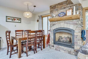 Un coin repas agrémenté d’une cheminée en pierre, de chaises en bois et d’un lustre.