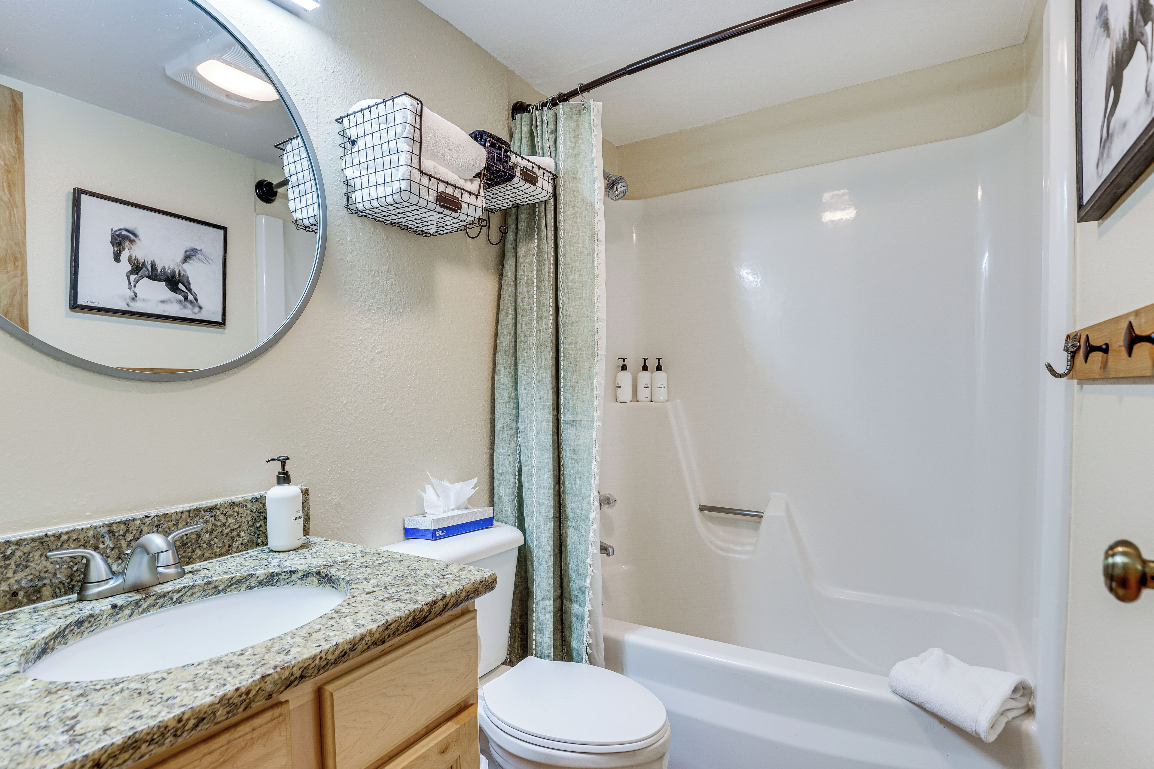 A bathroom with a sink, toilet, and bathtub. There is a shower curtain, a towel rack, and a framed picture on the wall.
