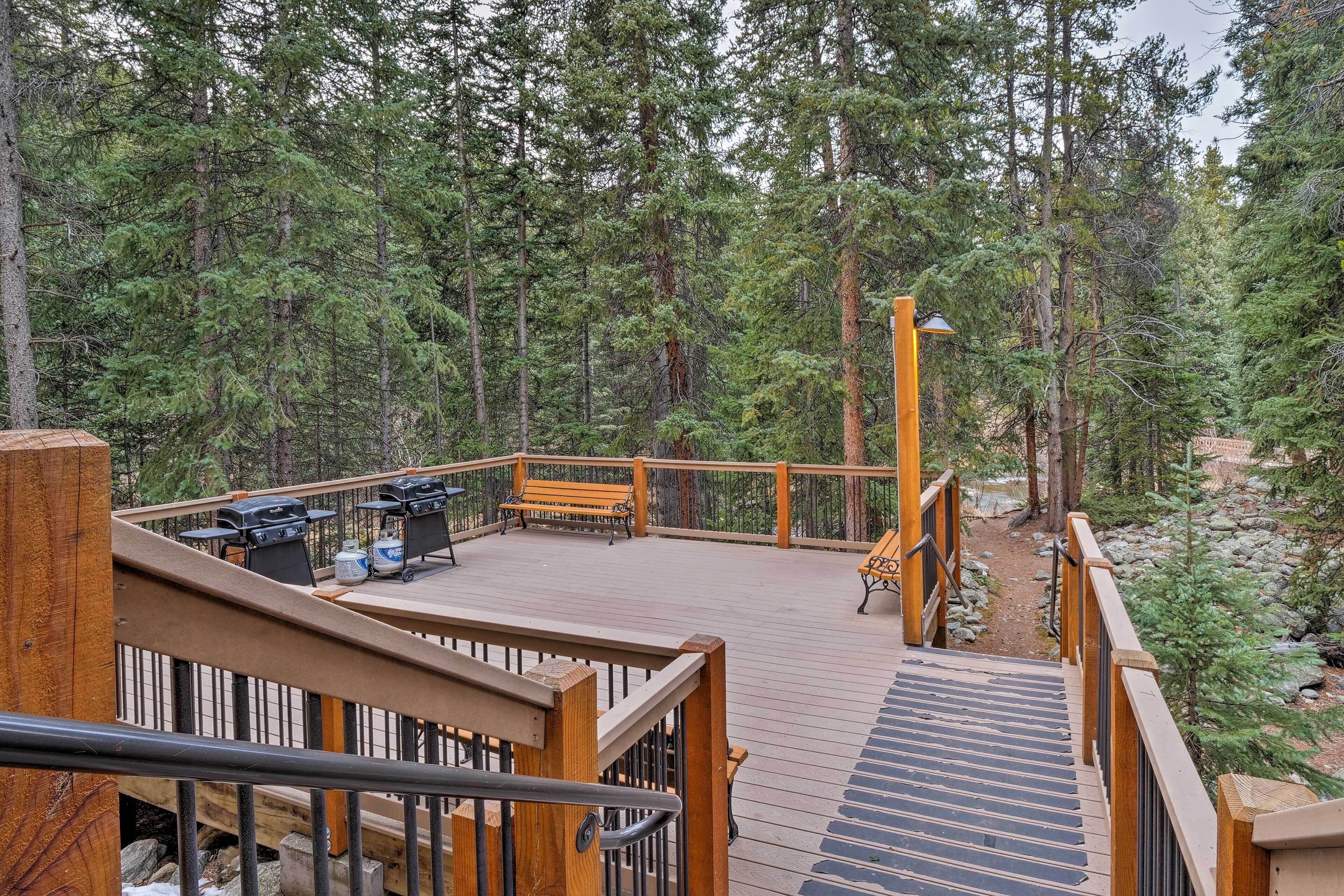Une terrasse en bois avec des sièges d’extérieur, entourée d’une forêt dense.