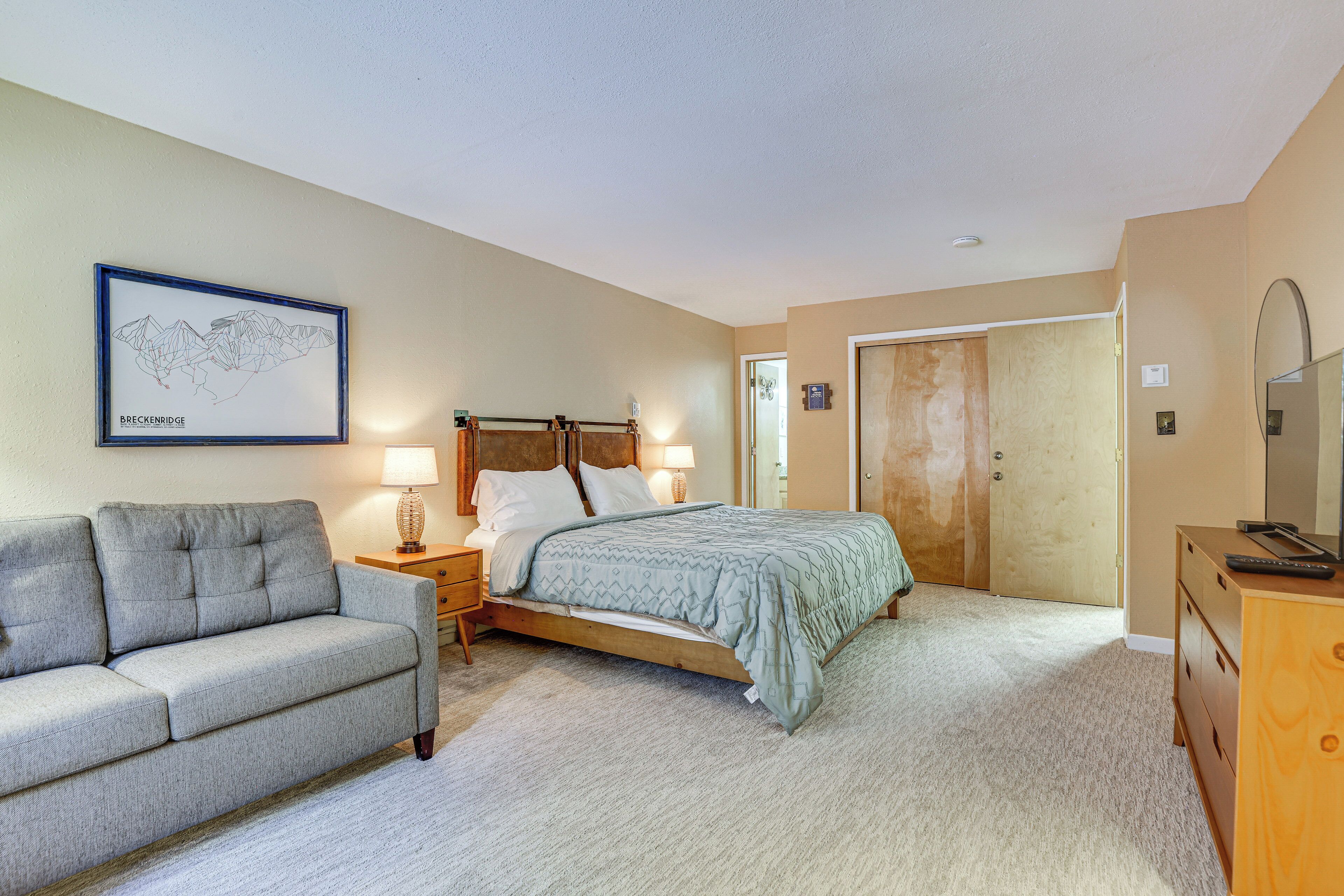 A bedroom with a bed, a nightstand, a dresser, a sofa, and a framed map on the wall.