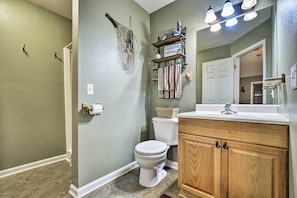 A bathroom with a toilet, wooden vanity, and a mirror. - Guntersville Lake Home w/ Deck & Covered Boat Slip (Scottsboro)