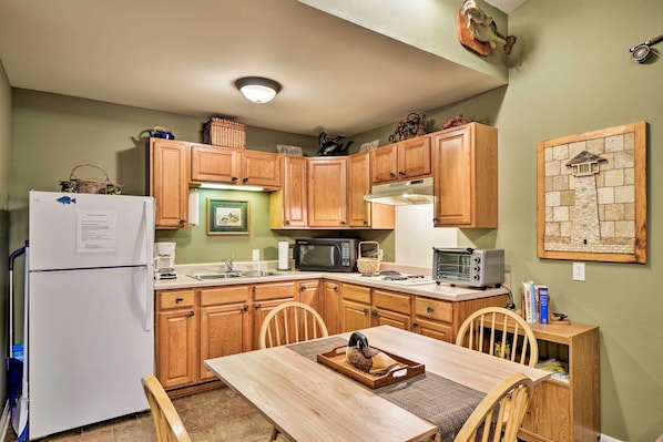 A compact kitchen with wooden cabinets, a refrigerator, microwave, and a dining table with chairs. - Guntersville Lake Home w/ Deck & Covered Boat Slip (Scottsboro)