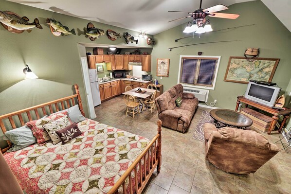 A cozy living room with a wooden bed, a brown sofa, and a dining area with a table and chairs. - Guntersville Lake Home w/ Deck & Covered Boat Slip (Scottsboro)