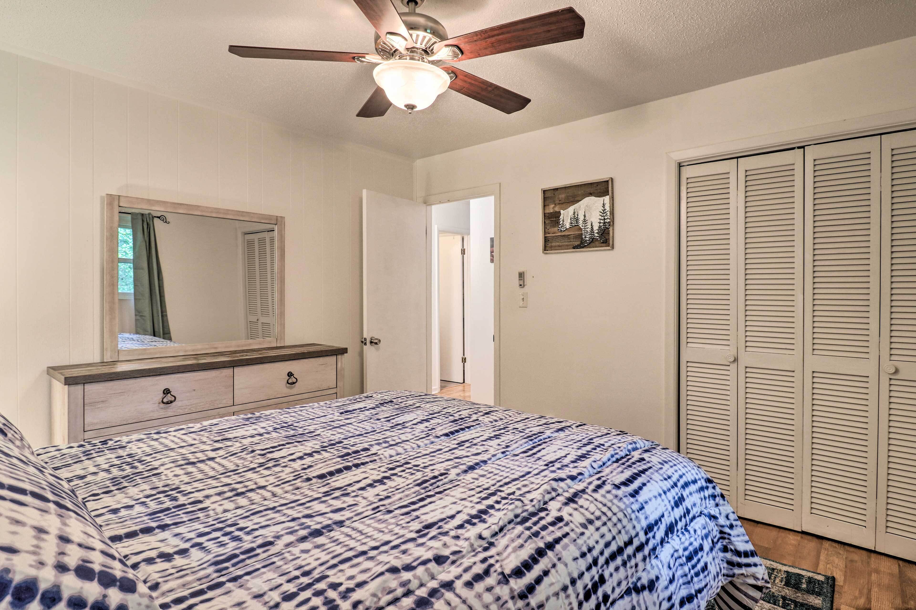 A bedroom with a bed, a ceiling fan, a dresser, a mirror, and a closet.